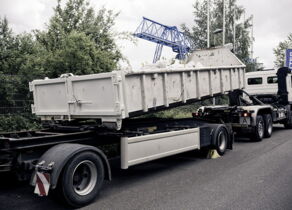 Abrollkipper setzt flachen Abrollcontainer auf Anhänger