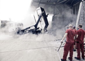 Muldenkipper kippt Bauschutt mit Staub und Mitarbeiter schauen zu