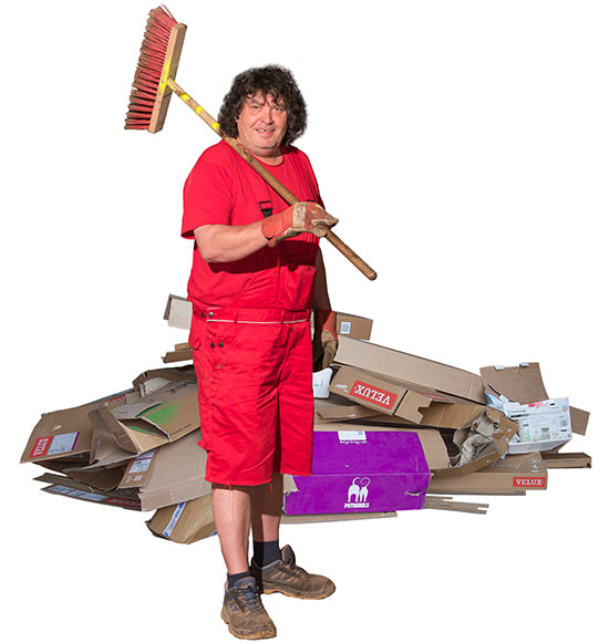 Mitarbeiter der Jörg Aulfinger GmbH & Co. KG in Rot mit Besen über der Schulter vor Haufen mit  Altpapier und Kartonagen