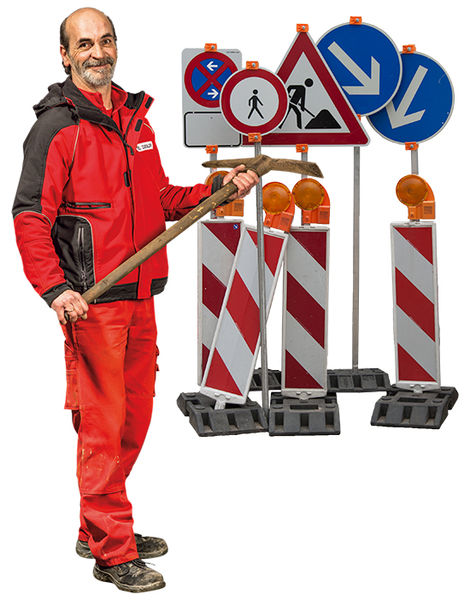 Aulfinger Mitarbeiter in Rot mit einer Harke über der Schulter, im Hintergrund mehrere Straßenschilder und Straßenabgrenzungen